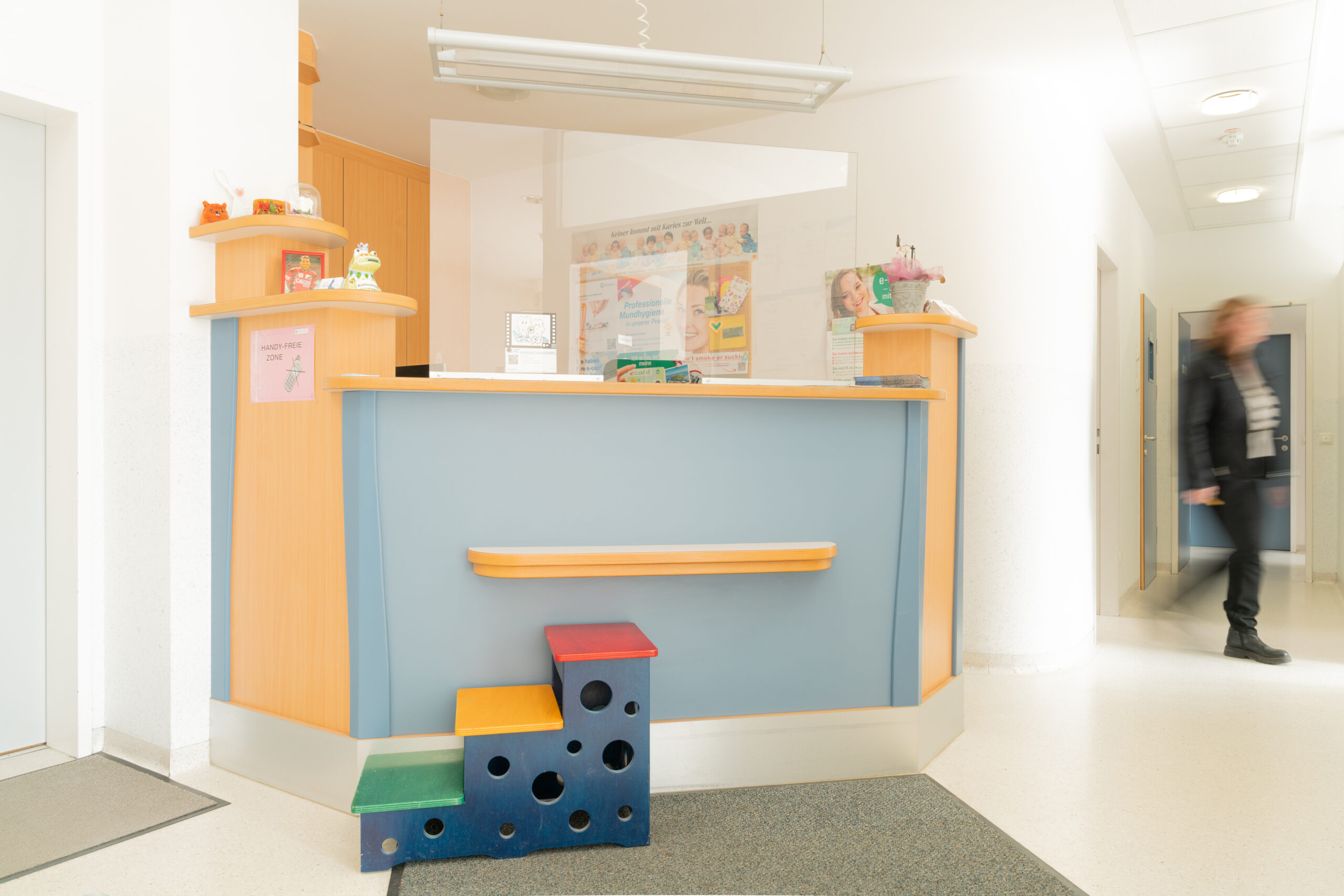 Eingangsbereich der Ordination. Eine Rezeption sowie eine bunte Kindertreppe zu ihr sind zu sehen